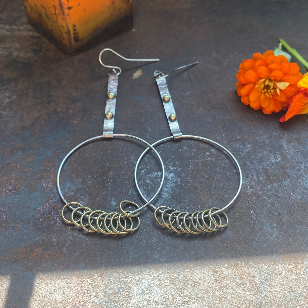 Handcrafted oversized sterling silver hoop earrings with textured silver bars, small brass accents, and interlocking brass rings by Zama Designz.