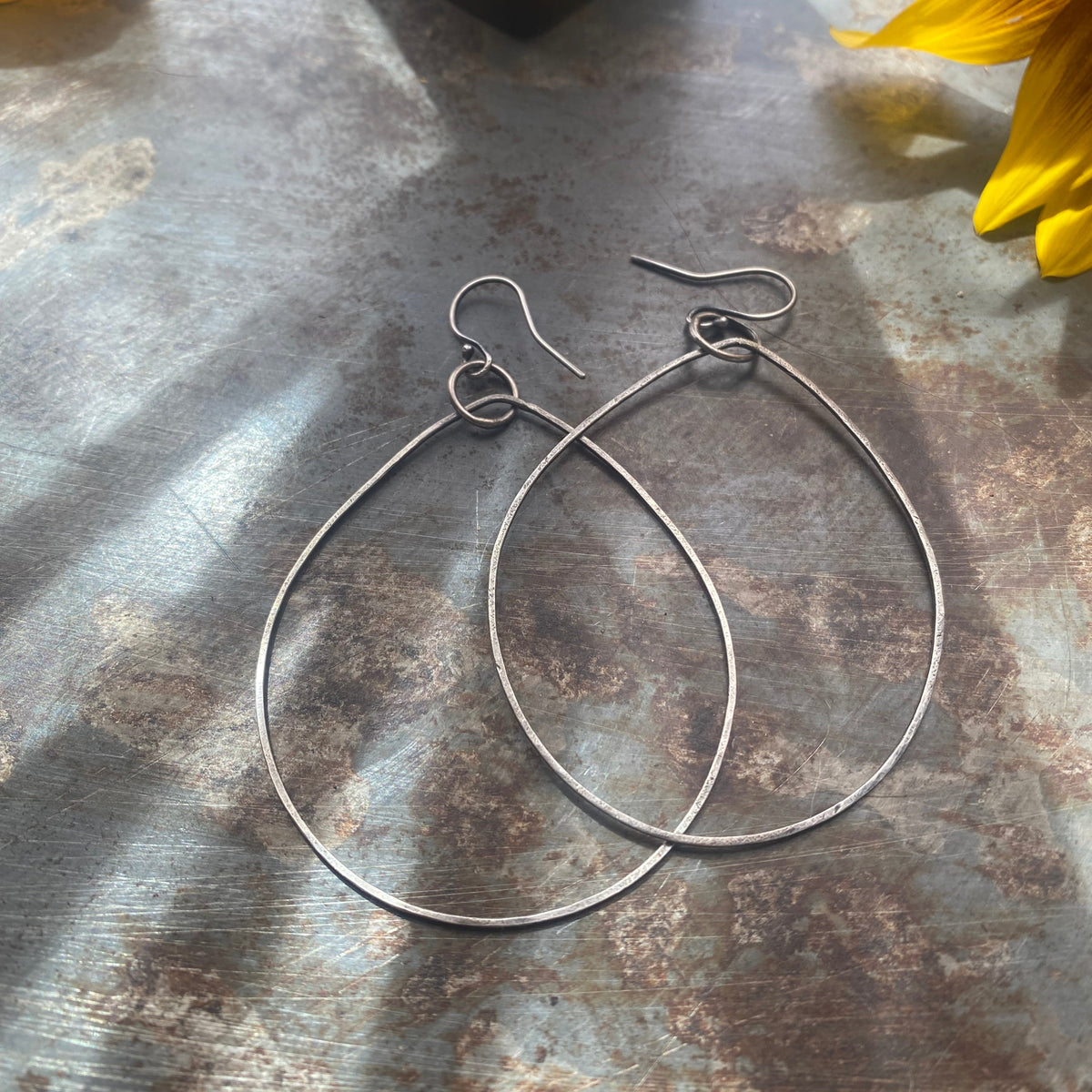Close-up of handmade sterling silver oval dangle earrings with organic sculptural design